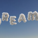 Schriftzug "DREAMS" aus Wolken an blauem Himmel gebildet.